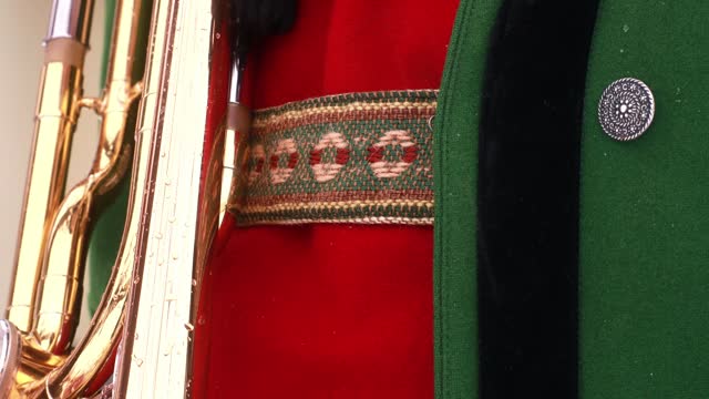 The upper part of a men's national costume, a thick green jacket, a red knitted vest and embroidered suspenders for leather trousers, holding a trombone