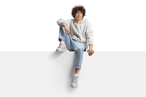 Guy with curly hair sitting on a panel and smiling isolated on white background