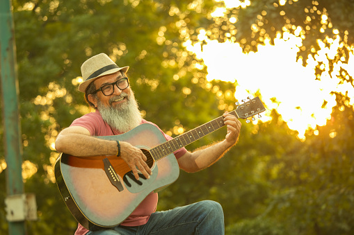 Ecstatic senior male playing guitar while spending leisure time in park during sunset