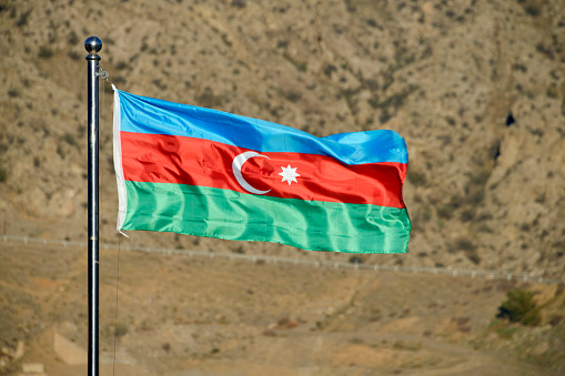 Khudafarin, Jabrayil Rayon, Azerbaijan: flag of Azerbaijan fluttering in the wind, seen against the hills across the Aras River in Iran. The national flag of the Republic of Azerbaijan is a blue-red-green tri-color divided horizontally, with a white crescent and an eight-pointed star (octagram) depicted in the middle stripe.