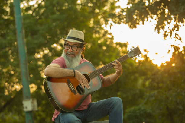Ecstatic senior male playing guitar while spending leisure time in park during sunset