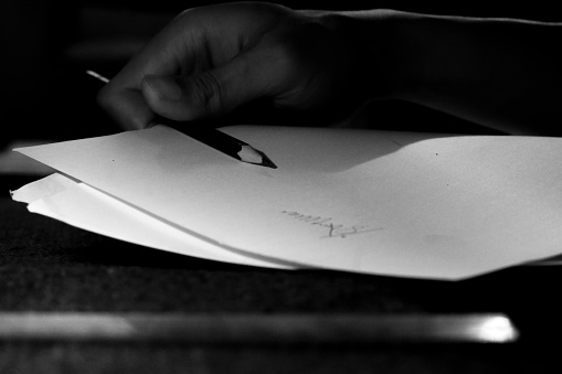 Monochrome image of a lawyer signing a legal document with an ink pen. Closeup view.