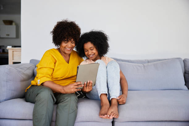 istock Smiling grandmother and young granddaughter using a tablet on a sofa 1919677554