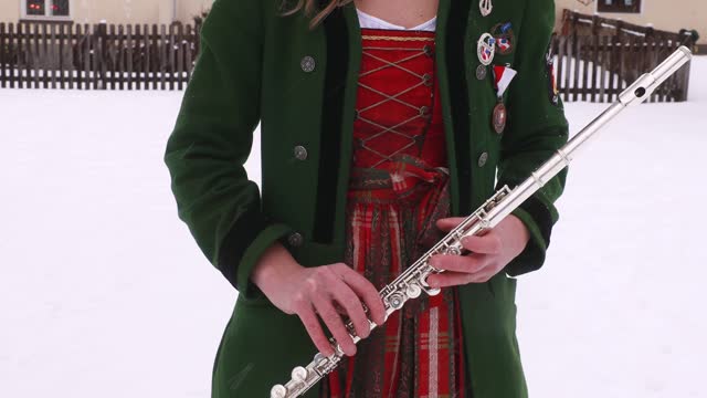 A young woman musician in traditional festive Austrian clothes holds a flute in her hands