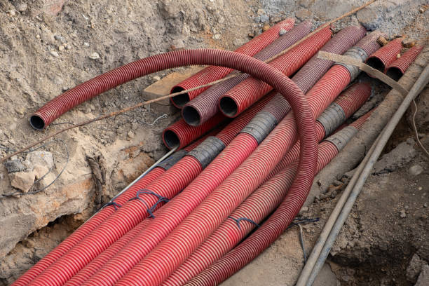 istock Network cables in red corrugated pipe are buried underground on the street. underground electric cable infrastructure installation. Construction site with A lot of communication Cables 1919720332