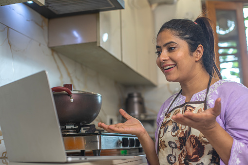 Woman working over laptop on countertop while cooking in kitchen at home