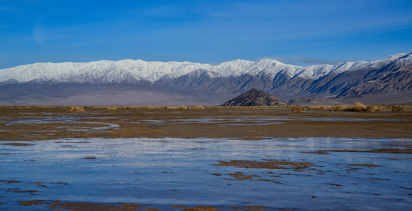 Landscape of wet clay desert in winter against the backdrop of snow-capped mountains in the Death Valley area, California