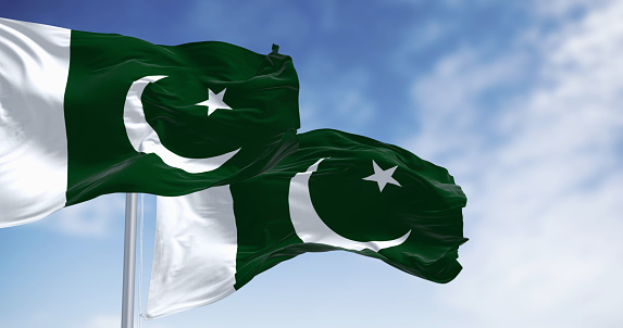 Two Pakistan National flags waving on a clear day. Green with white band on hoist; white crescent moon and five-pointed star. Seamless 3d render animation. Slow motion loop. Selective focus
