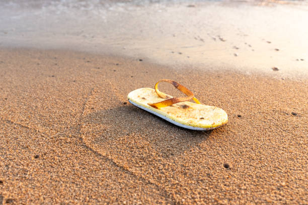 une vieille sandale jaune en mousse de polyuréthane est laissée sur la plage par une personne imprudente, ce qui pose un problème environnemental - disposable cup plastic beer bottle photos et images de collection