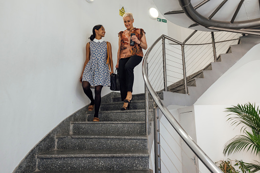 A wide angle view of two female co workers leaving the office they work at in Newcastle Upon Tyne in the North East of England. They have finished for the day and are walking down the spiral staircase together.