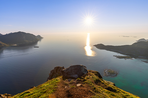 From the vantage point of Offersoykammen, the sun's rays stretch across the water, casting a brilliant sheen over the landscape of the Lofoten Islands at midnight