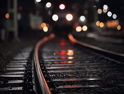 A close-up of a train moving along a set of tracks on a damp, dark night