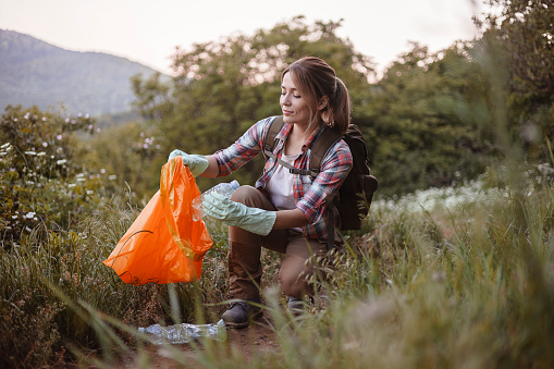 Volunteer cleaning up the forest, she is collecting trash and holding a garbage bag, environmental protection concept