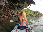 Young woman kayaking in tropical setting, rear view from friend's perspective