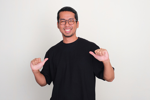 Adult Asian man pointing to plain black t-shirt that he wearing with happy expression