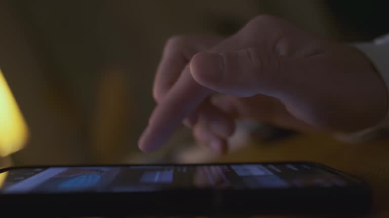 Man's finger flips through a tape of pictures in a smartphone. Side view, close-up, inside a dark room. The end of flipping the tape, removes his hand.