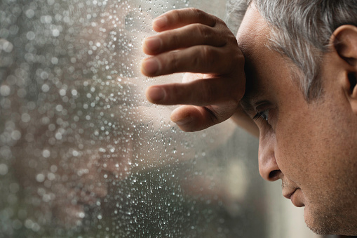 Man looking out of window at rainy day.