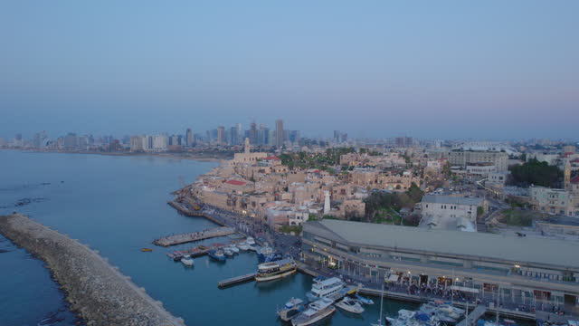 Wide parallax view drone shot of Old city of Jaffa and Jaffa port at sunset with lots of families visiting restaurants, shops and bars in the port - tel aviv city at the background