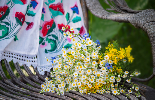 A bouquet of wildflowers against a background of embroidered towels on an old wicker chair in the garden. traditional Ukrainian embroidery. Rural still life