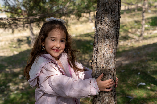 Little girl on the shore of a lake grabbing an insect from a tree branch. Girl in love with wildlife, enjoying a day in nature.