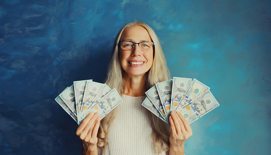 Portrait of happy smiling middle aged woman holding cash money in dollar bills in her hands