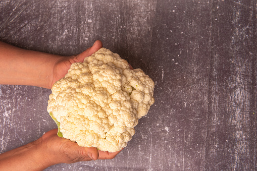 Un Toque de Frescura: Manos que Sostienen un Coliflor sobre una Mesa de Madera Clara