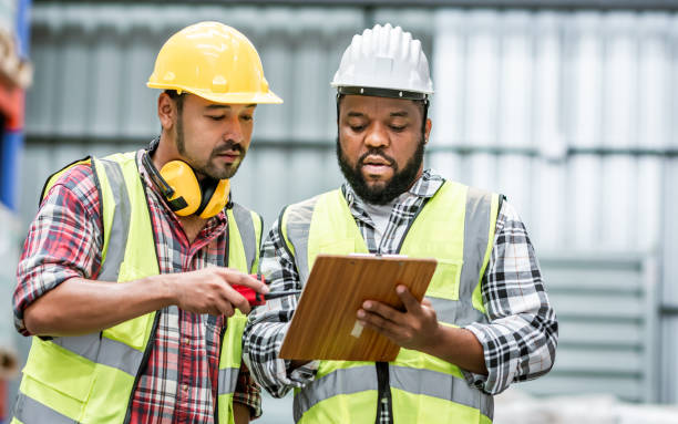 istock Two diverse professional male workers holding board, checking shipping stocks in storage, warehouse or factory for delivery, wearing safety hat. Diversity, Commercial Industry Business Concept. 1920024637
