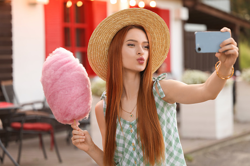 Funny woman with cotton candy taking selfie outdoors