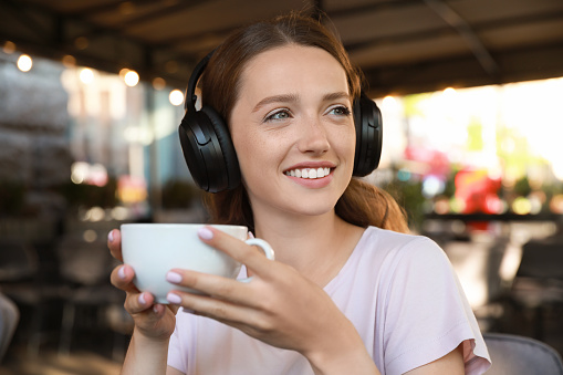 Smiling woman in headphones drinking coffee outdoors