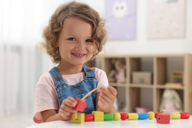 istock Motor skills development. Little girl playing with wooden pieces and string for threading activity at table indoors 1920093192