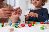 Motor skills development. Father and daughter playing with wooden pieces and strings for threading activity at table indoors, closeup