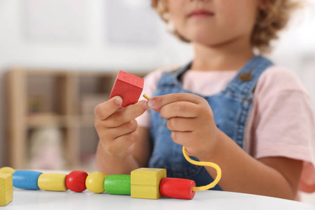 istock Motor skills development. Little girl playing with wooden pieces and string for threading activity at table indoors, closeup 1920093730