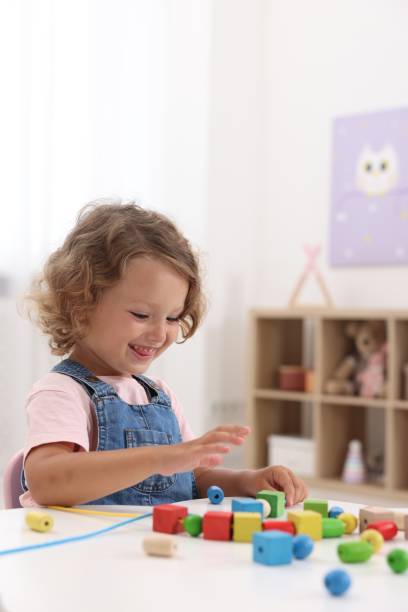 istock Motor skills development. Little girl playing with wooden pieces and string for threading activity at table indoors 1920095354