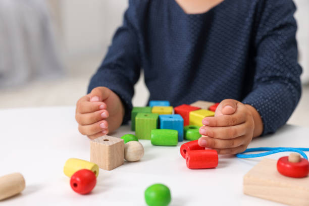 istock Motor skills development. Little girl playing with wooden pieces and string for threading activity at table, closeup 1920096629