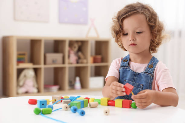 istock Motor skills development. Little girl playing with wooden pieces and string for threading activity at table indoors 1920105405