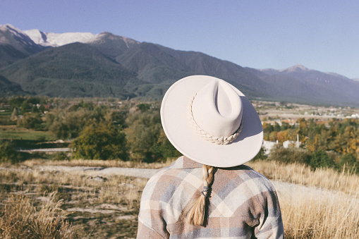 A woman stands in a meadow and looks at the mountains.