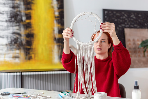 Boho style. Braided strings. Woman craftsman weaves macrame from light cotton threads.