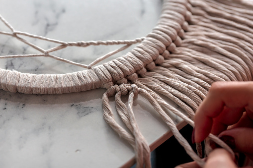 Boho style. Braided strings. Woman craftsman weaves macrame from light cotton threads.