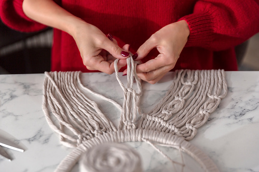 Boho style. Braided strings. Woman craftsman weaves macrame from light cotton threads.