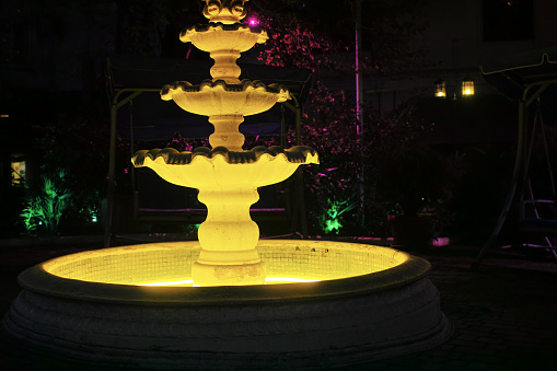 a plaster retro fountain illuminated at night, urban scene