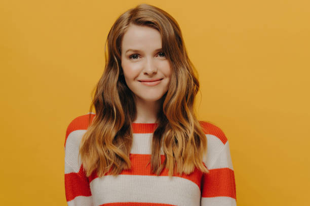 istock Smiling woman with flowing hair wearing a striped sweater, her contented expression a burst of warmth against a yellow backdrop. 1920181237