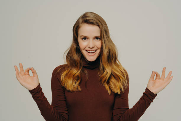 istock Confident woman in a brown turtleneck making OK gestures with both hands, her joyful demeanor against a neutral background 1920181746