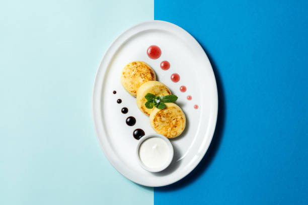 istock Cheesecakes from homemade cheese with sour cream and jam on a light ceramic plate. Place the plate on a colored paper background. 1920196512