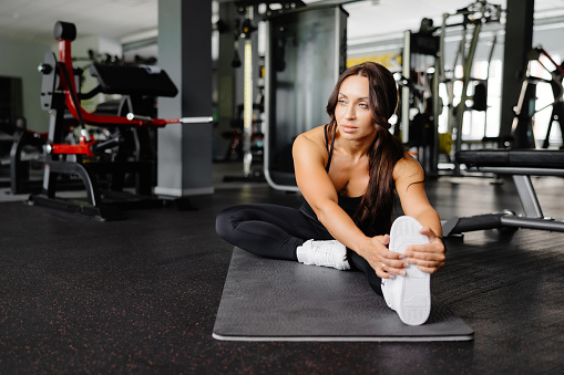 Woman is stretching body in gym. portrait and sport preparation. Young woman is stretching her leg in gym.