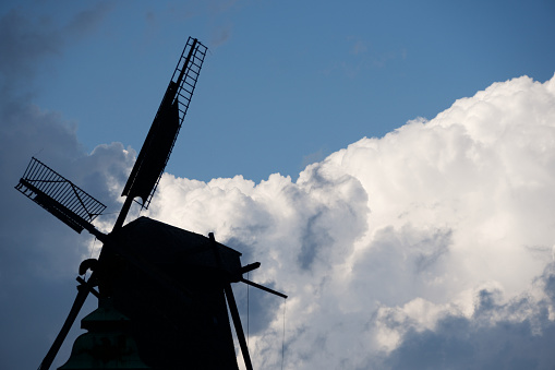 The stark silhouette of a traditional windmill stands out against the dramatic cloudscape, evoking the rural history within Potsdam's evolving landscape.
