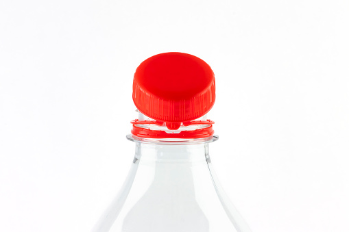 Red tethered cap on beverage bottle. Mandatory attached cap on bottle in EU ensuring that bottles and caps recycled together . Reducing litter.