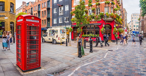 People walking through Covent Garden, London, past iconic red telephone box, ice cream van and flower-festooned traditional pub.