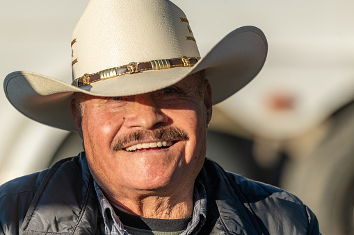 Smiling senior Hispanic man looking at camera wearing a cowboy hat