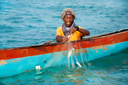 Morondava,Madagascar . 18 october 2023. Malagasy fisherman on homemade wooden old pirogue boat in ocean catches fish with net. selective focus, close-up view from ocean