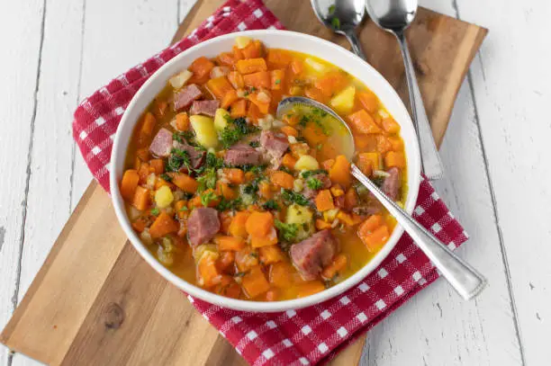Delicious carrot stew or carrot soup with potatoes, vegetables and smoked pork meat on a plate with spoon. closeup with copy space
